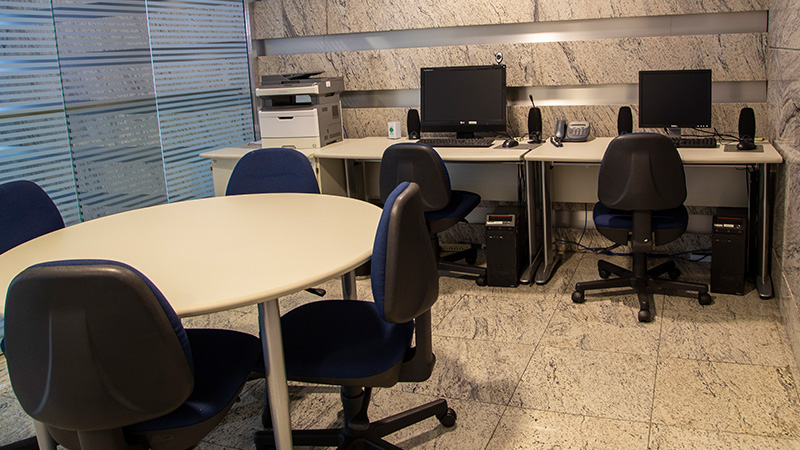 Sala de apoio do Teatro CIEE, com uma mesa redonda e cadeiras ao redor. Ao fundo, uma impressora e dois computadores