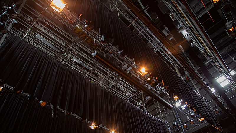 Foto mostrando os diversos equipamentos, como vestimentas cênicas, iluminação na parte superior do palco.