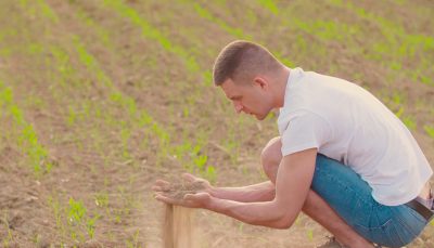 Jovem agachado no campo segurando um punhado de terra na mão enquanto olha para ela.