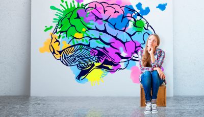 Garota sentada e observando um quadro ao fundo com uma ilustração de um cérebro com diversas partes coloridas