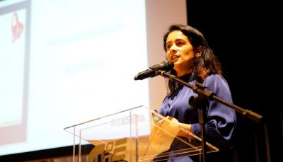 mulher vestida de azul, falando ao microfone em palco