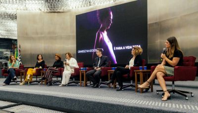 seis mulheres e um homem em palco, sentados em cadeiras