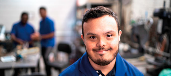 #PraCegoVer #ParaTodosVerem #DescriçãoDaImagem: Um rapaz com uma camisa azul com síndrome de down sorrindo num ambiente de trabalho. Fim da descrição.
